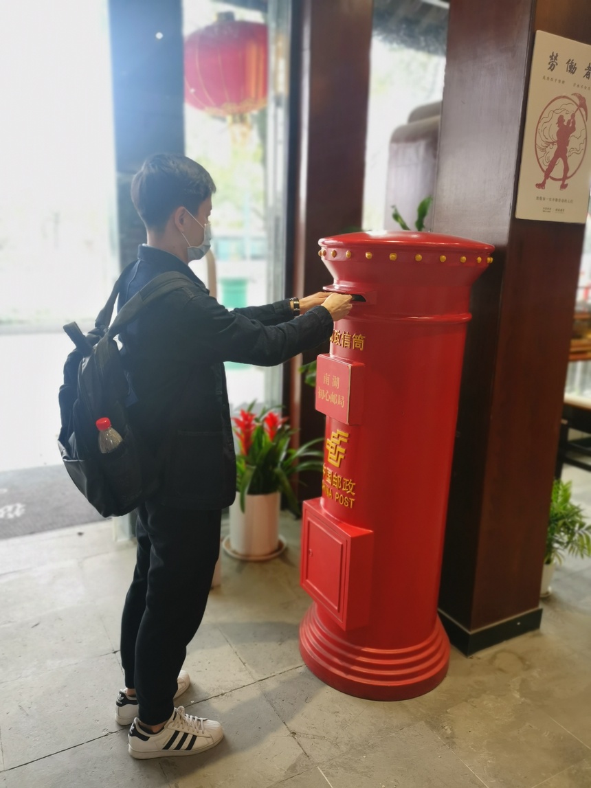 游客正在往红色邮筒投递明信片(嘉兴市南湖名胜区供图)